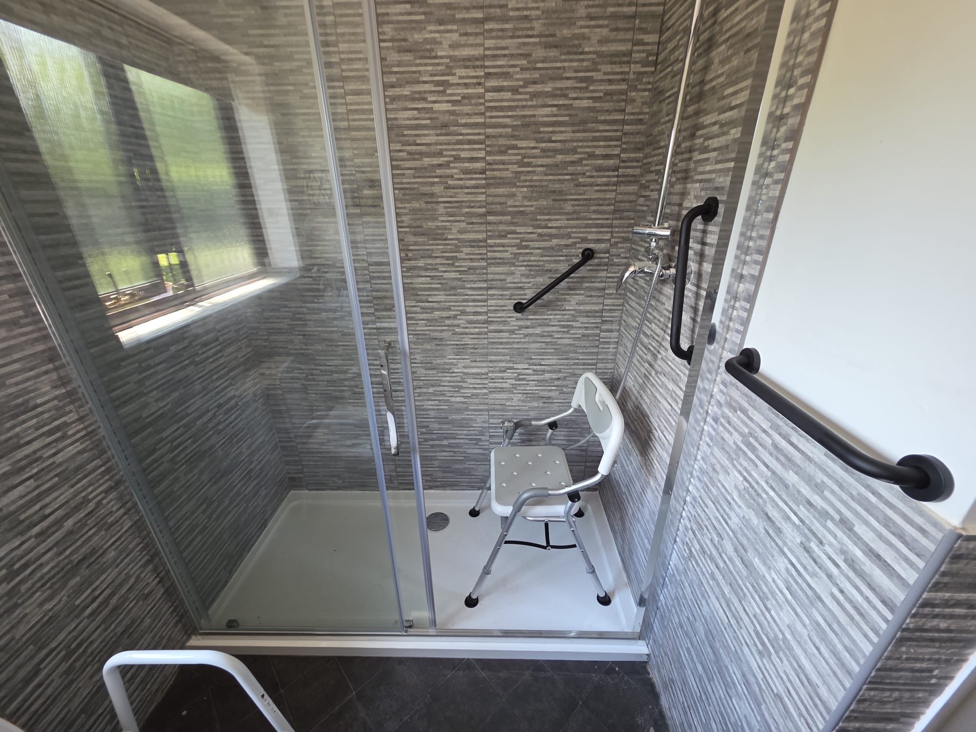 Newly installed walk-in shower enclosure with grab rails and shower seat