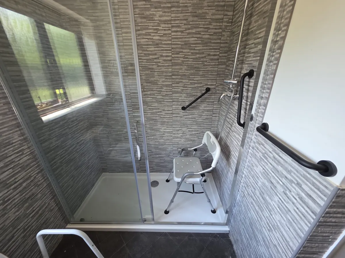 Newly installed walk-in shower enclosure with grab rails and shower seat